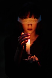 blindfolded Figure only lit by the candle they are holding towards the camera